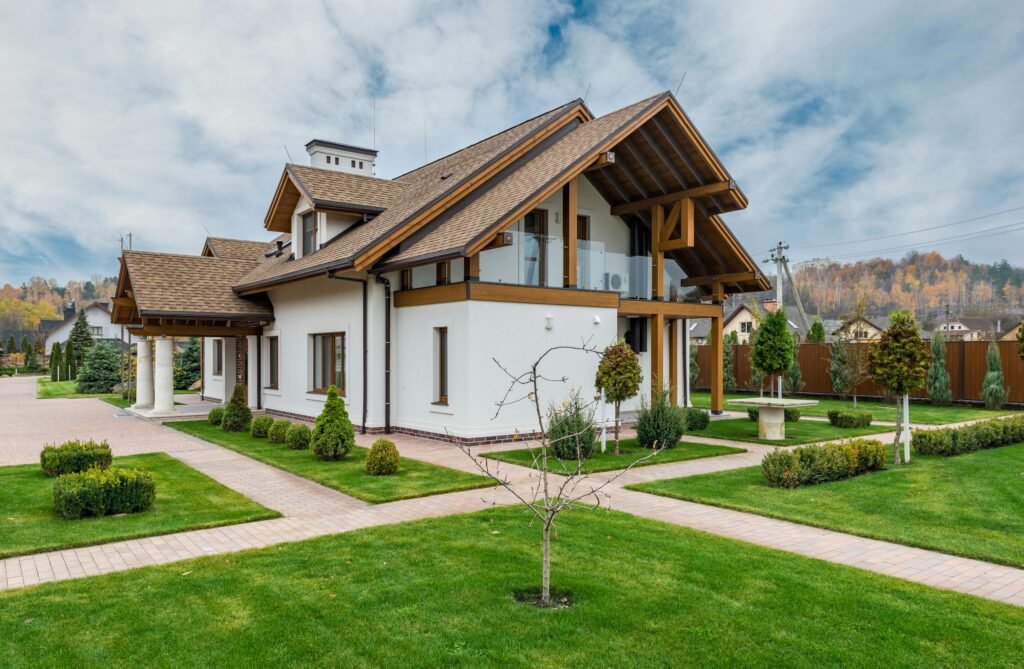 Exterior of modern cottage house with columns and balcony surrounded by green grass and trees